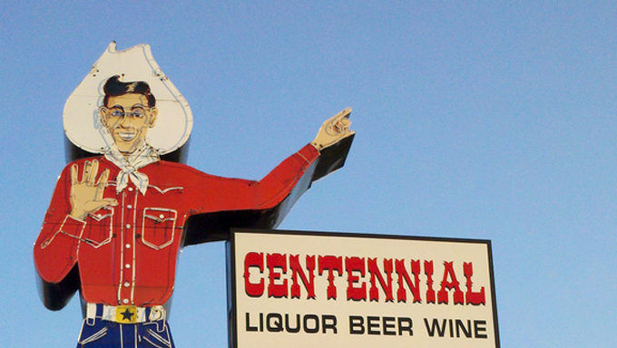 A liquor store sign includes Big Tex pointing towards its entrance. 