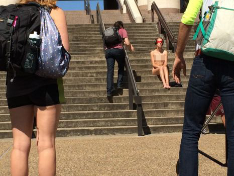 Student sitting naked on campus steps while fellow peers walk by. 
